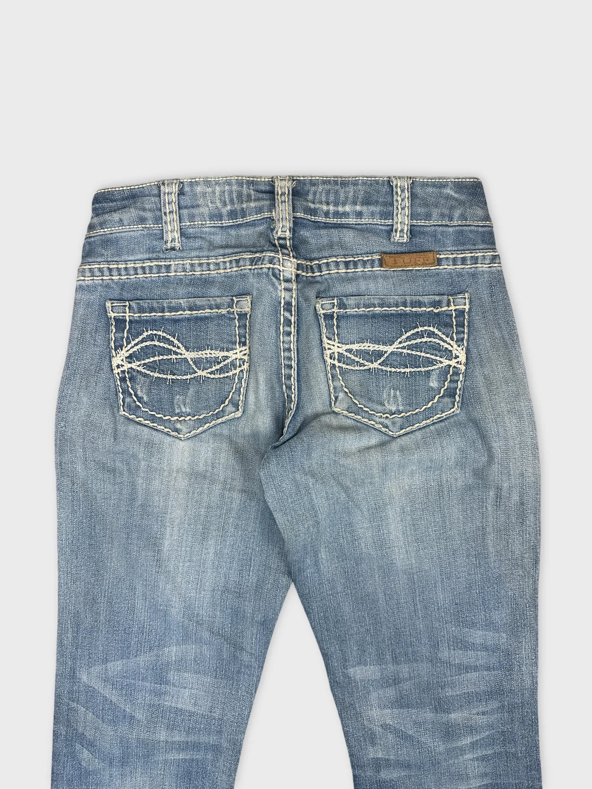 Detail view of women's denim jeans in light blue with decorative back pockets.