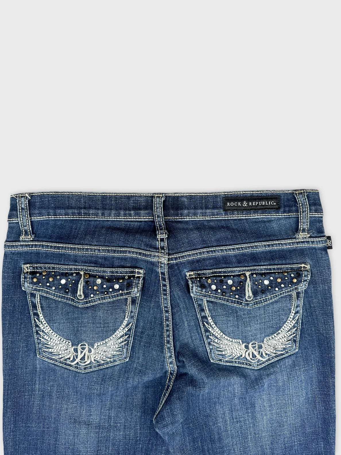 Detail view of blue denim jeans with embellished back pockets.