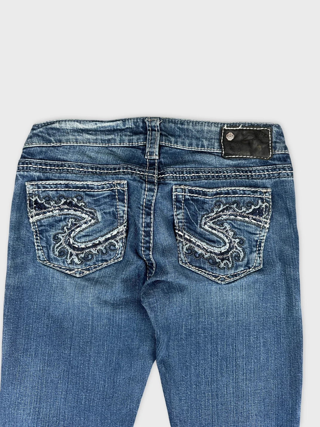 Detail view of blue denim jeans featuring embroidered back pockets.
