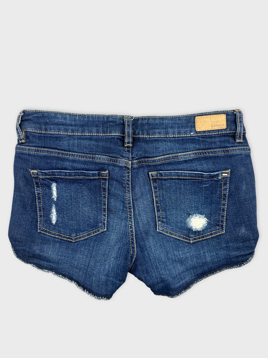 Back view of women denim shorts in dark blue with frayed hem.