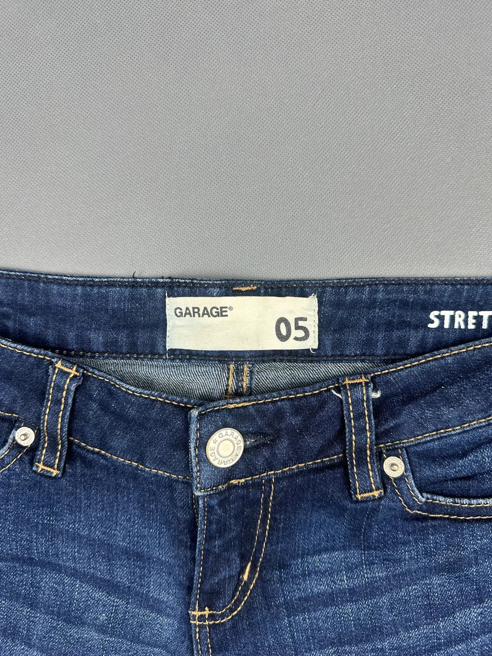 Detail view of women denim shorts in dark blue with visible button and stitching.