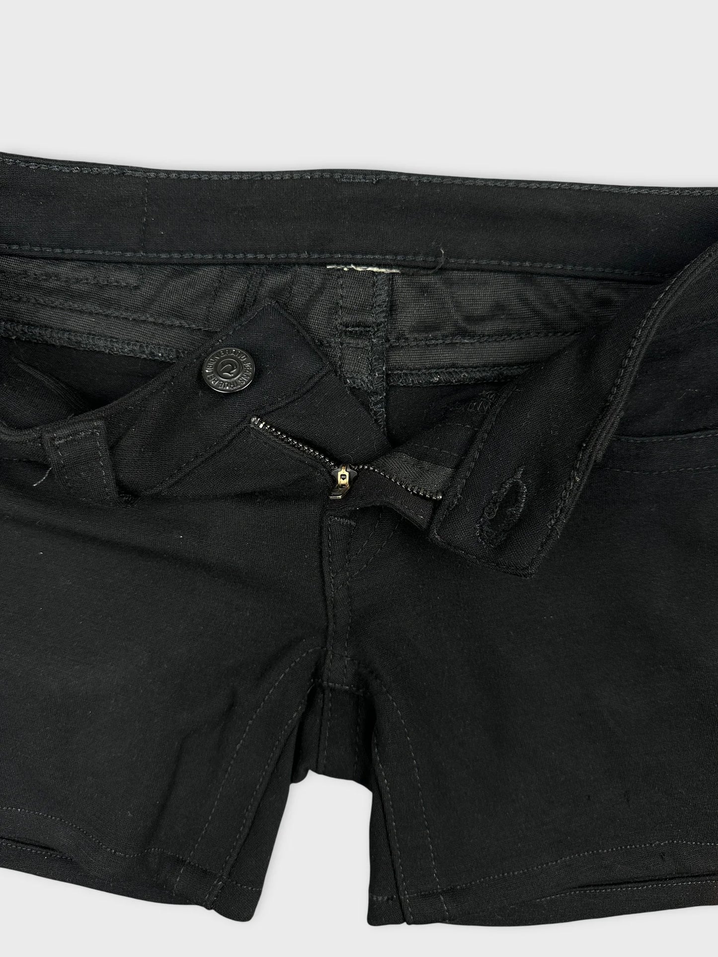 Detail view of black denim shorts featuring a zip and button closure.