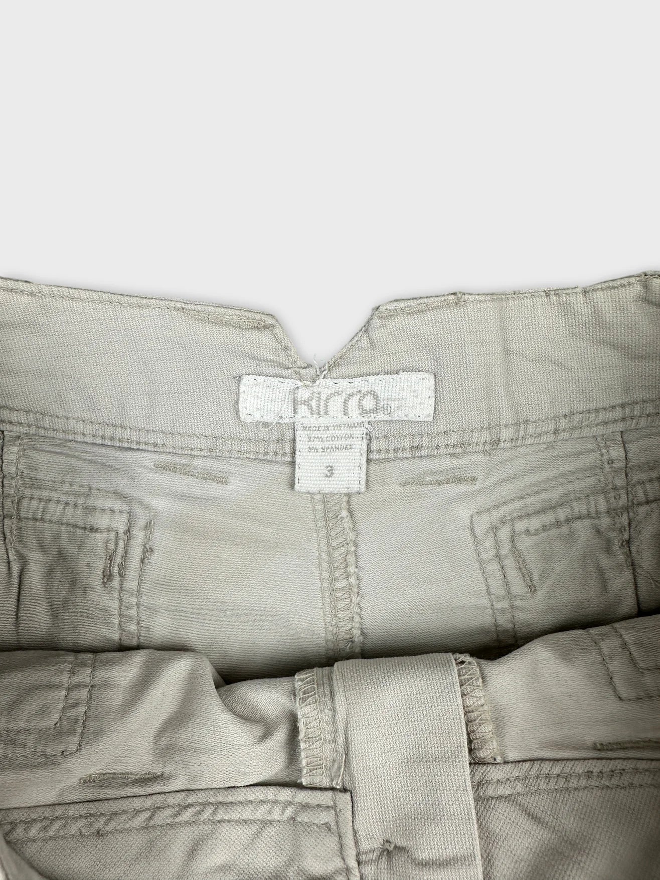 Detail view of beige denim shorts featuring a belt loop and tag.