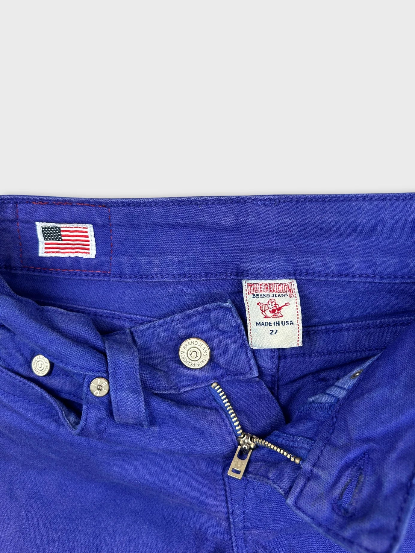 Detail view of blue denim shorts featuring a zip fly and button closure.