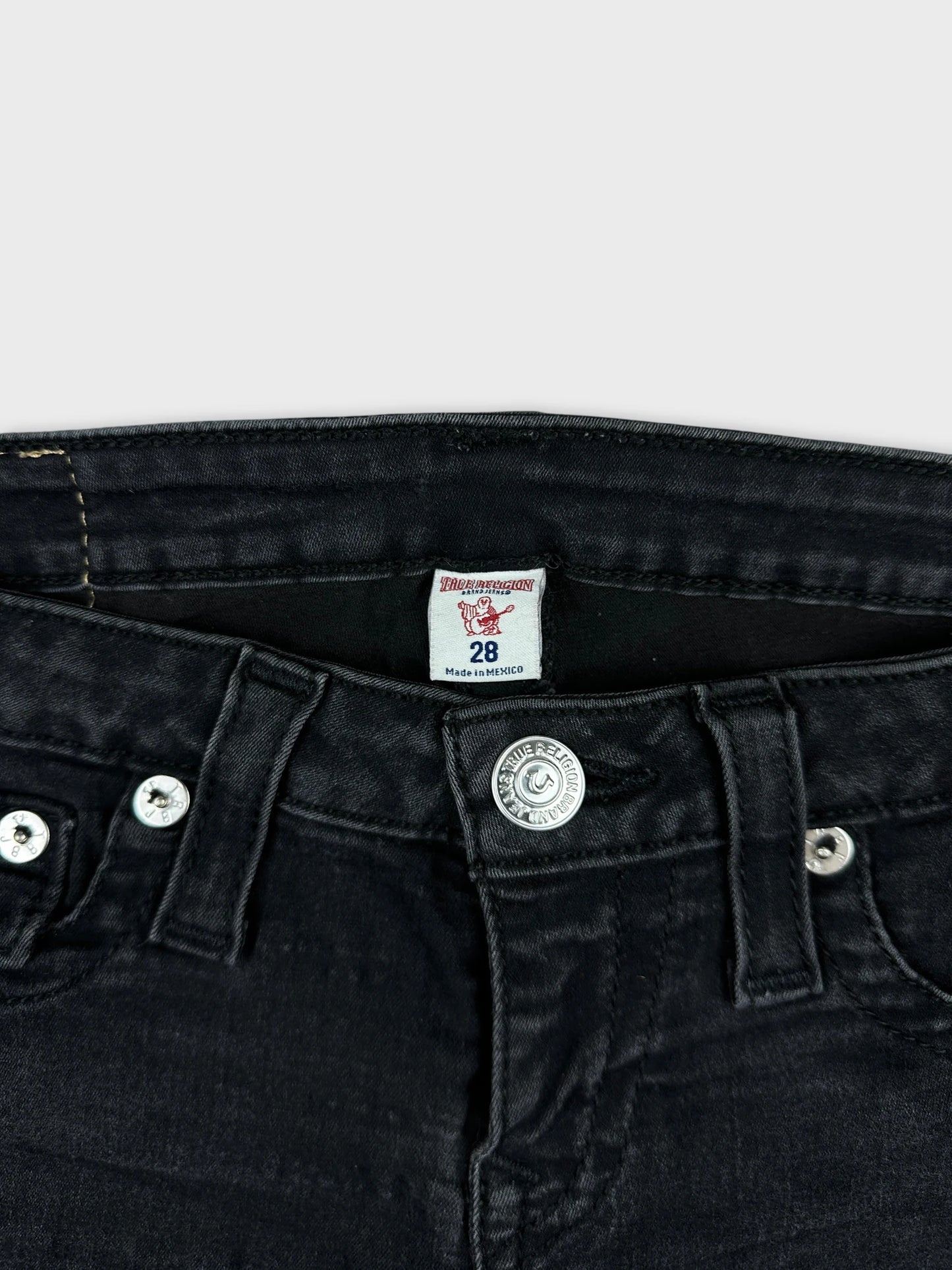 Detail view of black denim shorts with silver buttons and stitching.