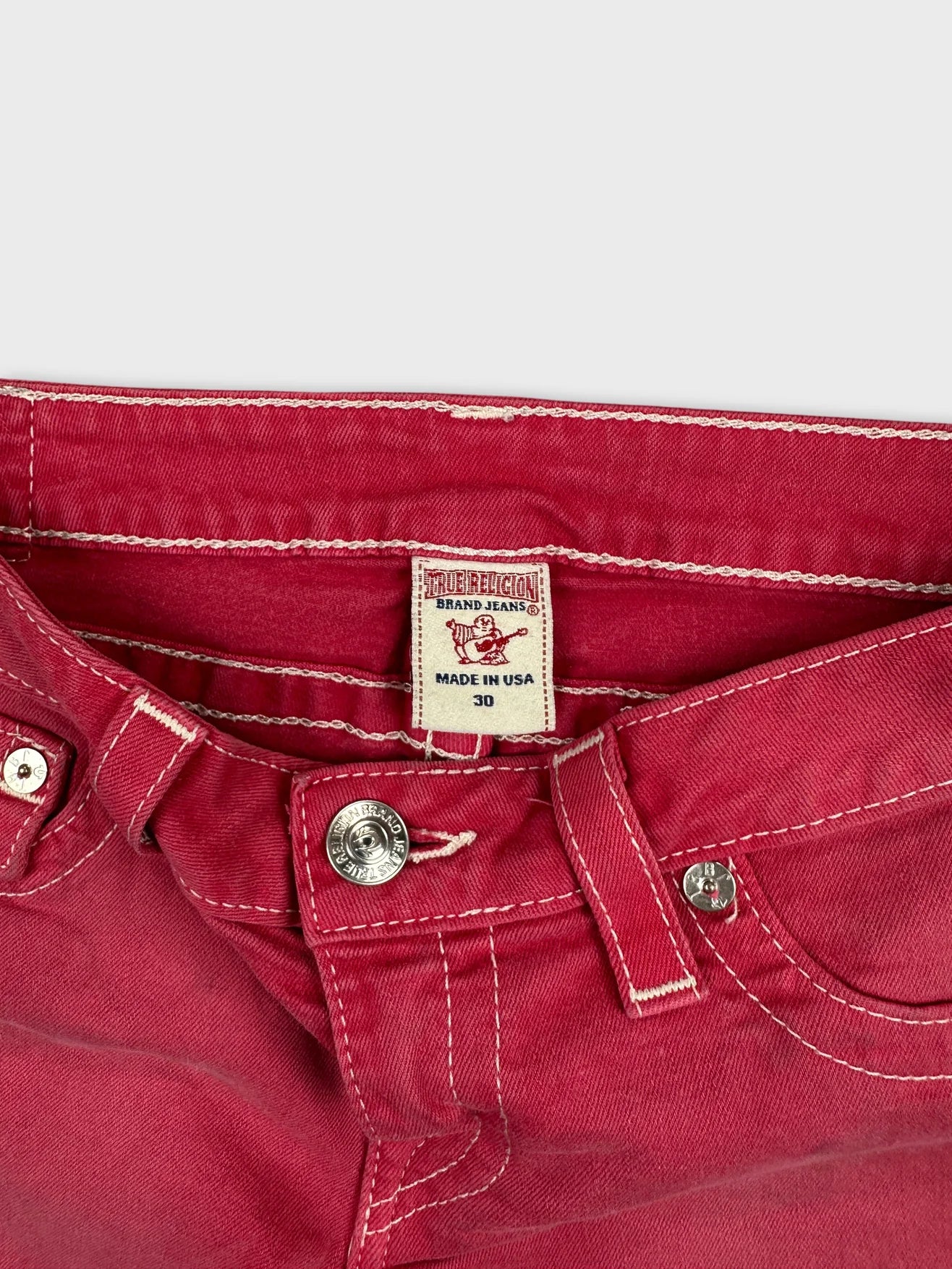 Detail view of red denim shorts featuring a metal button and white stitching.