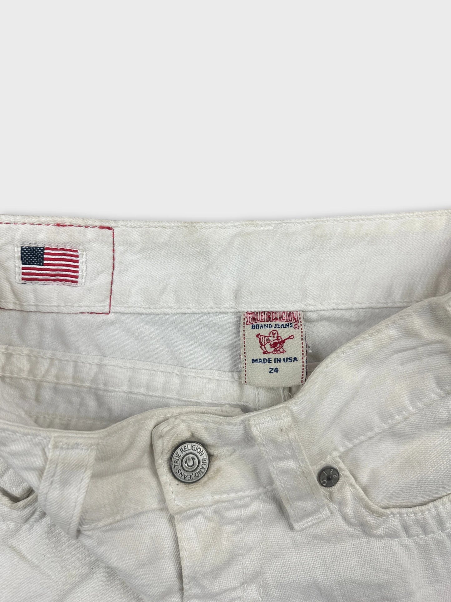 Detail view of white denim shorts featuring a flag patch and button detail.