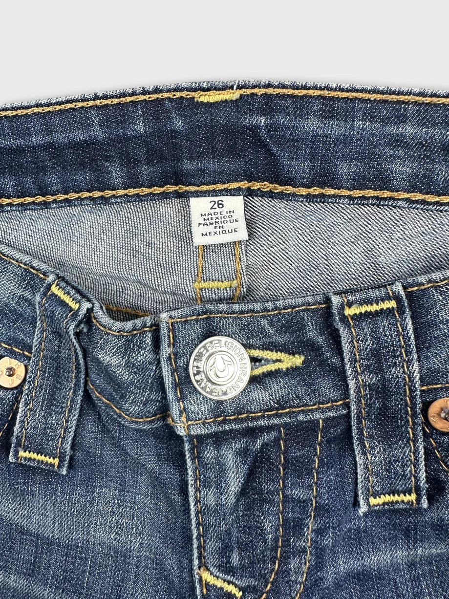Detail view of women denim shorts in dark blue with brass button and yellow stitching.