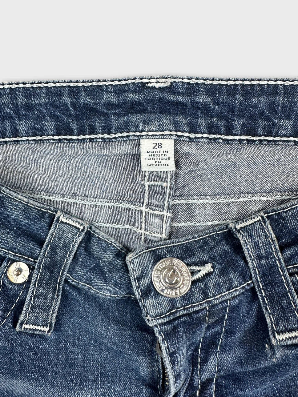 Detail view of women denim shorts featuring a dark blue color and metal button.