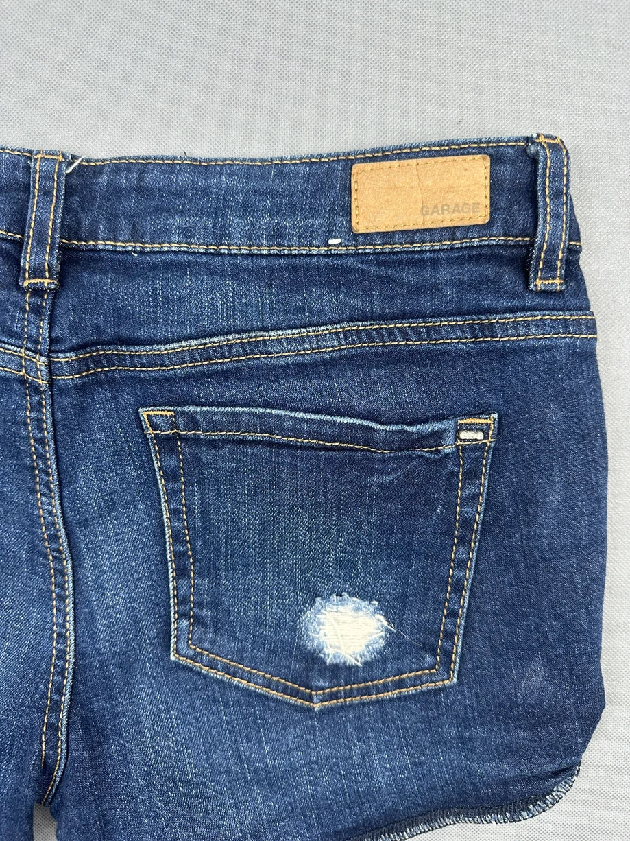 Detail view of dark blue denim shorts with distressed pocket.