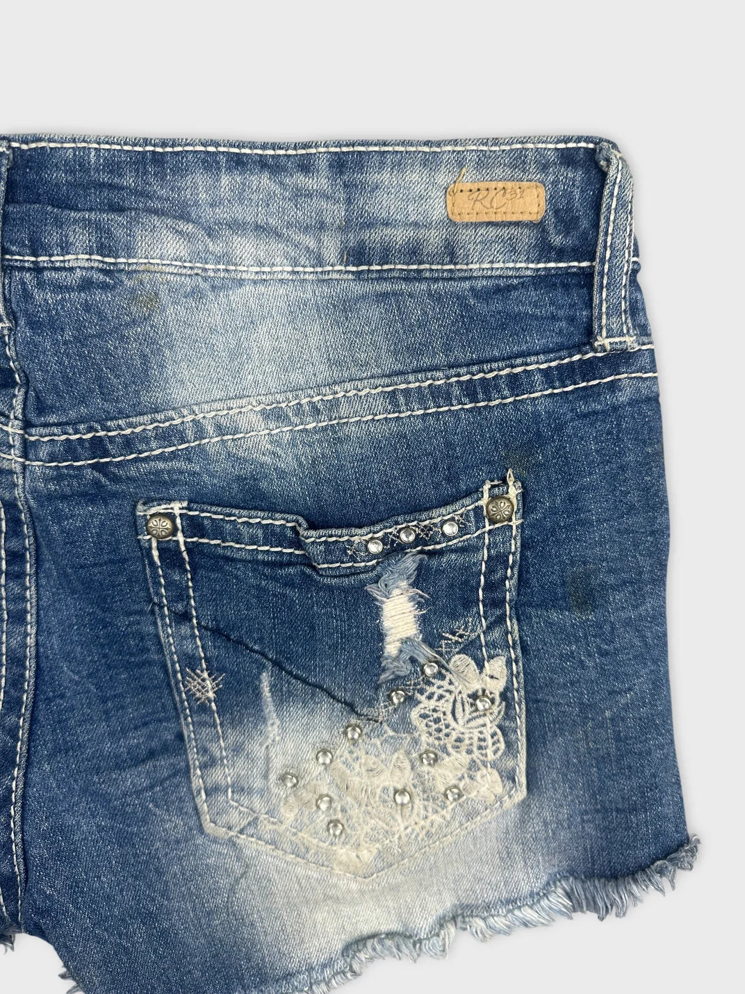 Detail view of blue denim shorts with embellished back pocket design.