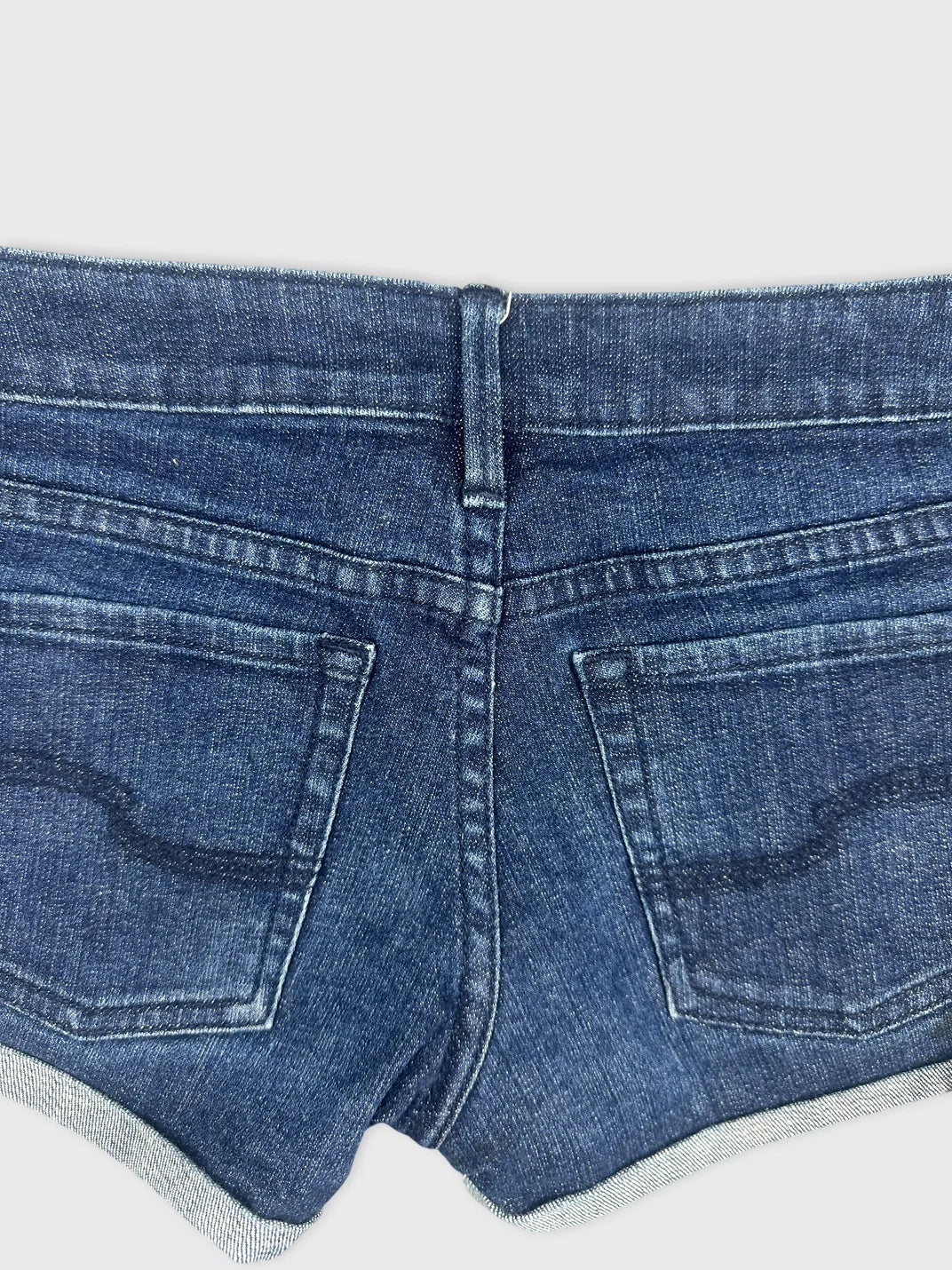 Detail view of women denim shorts in dark blue with back pockets.