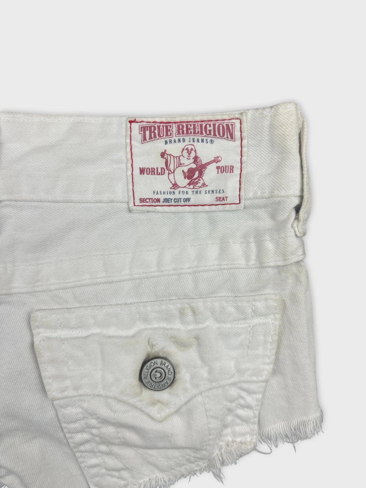 Detail view of white denim shorts with a branded tag and pocket button.