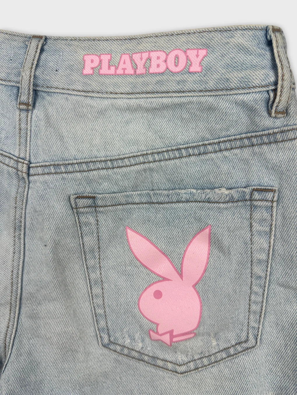 Detail view of denim shorts featuring a pink Playboy logo on the back pocket.