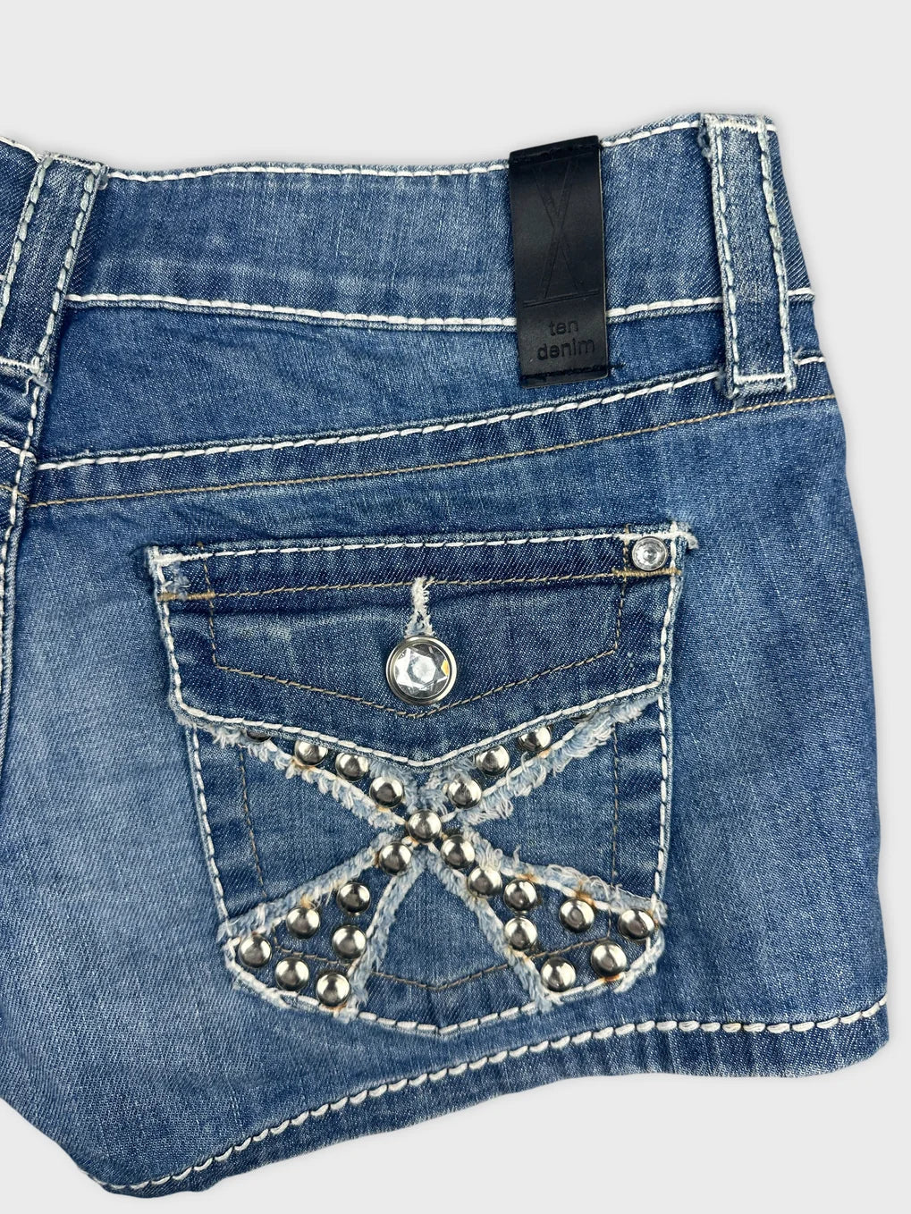 Detail view of blue denim shorts with studded pocket design.