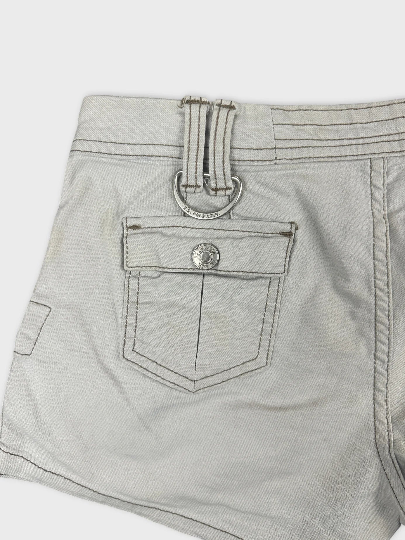Detail view of white denim shorts featuring a ring and back pocket.