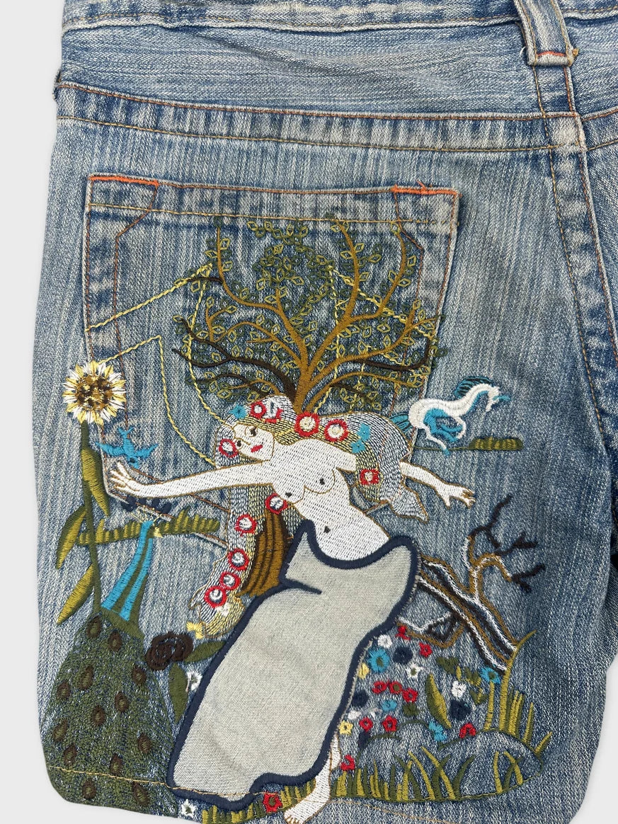 Detail view of denim shorts featuring a colorful embroidered design of a woman and trees.