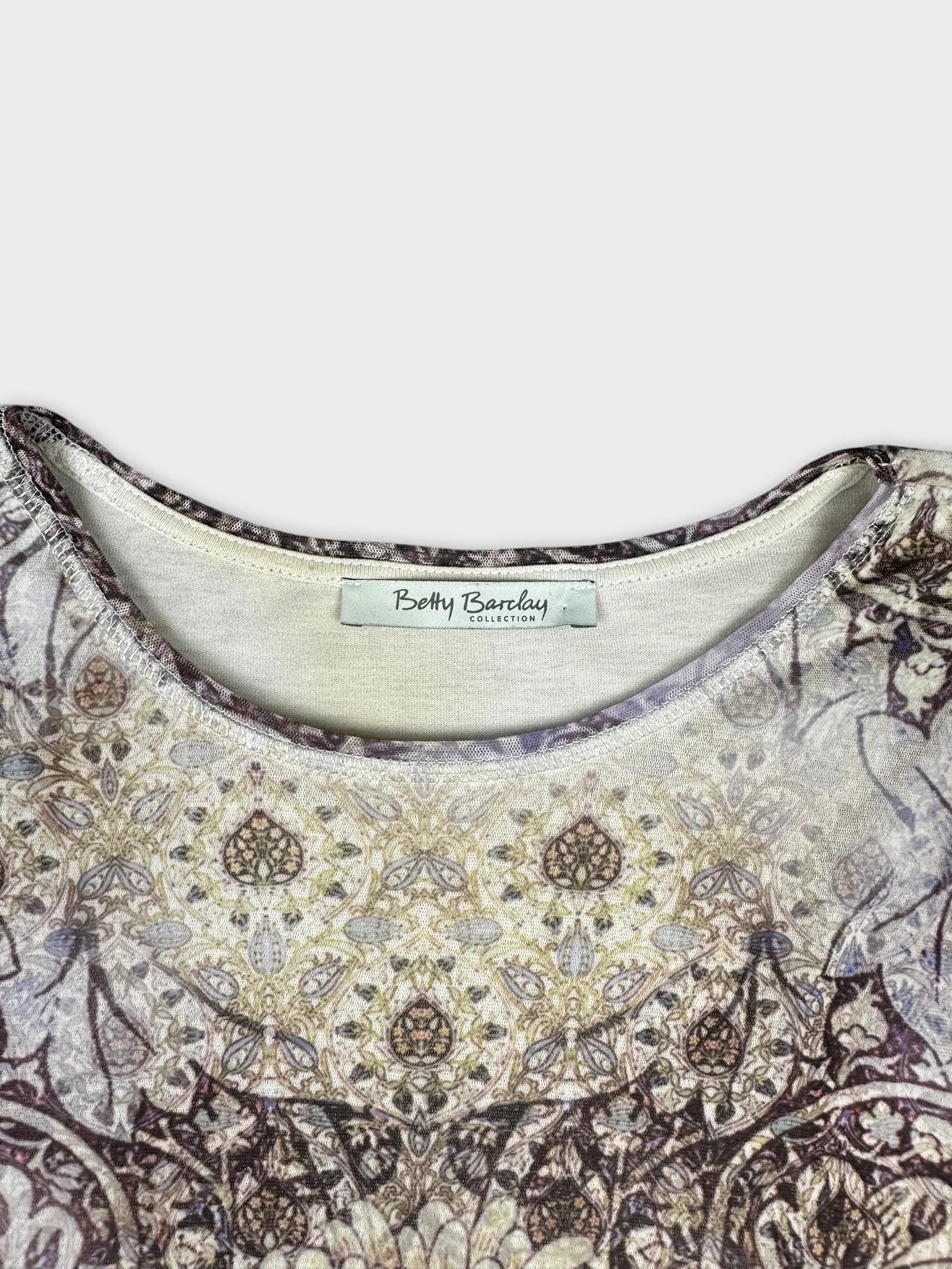 Detail view of a long sleeve shirt in cream with intricate pattern.
