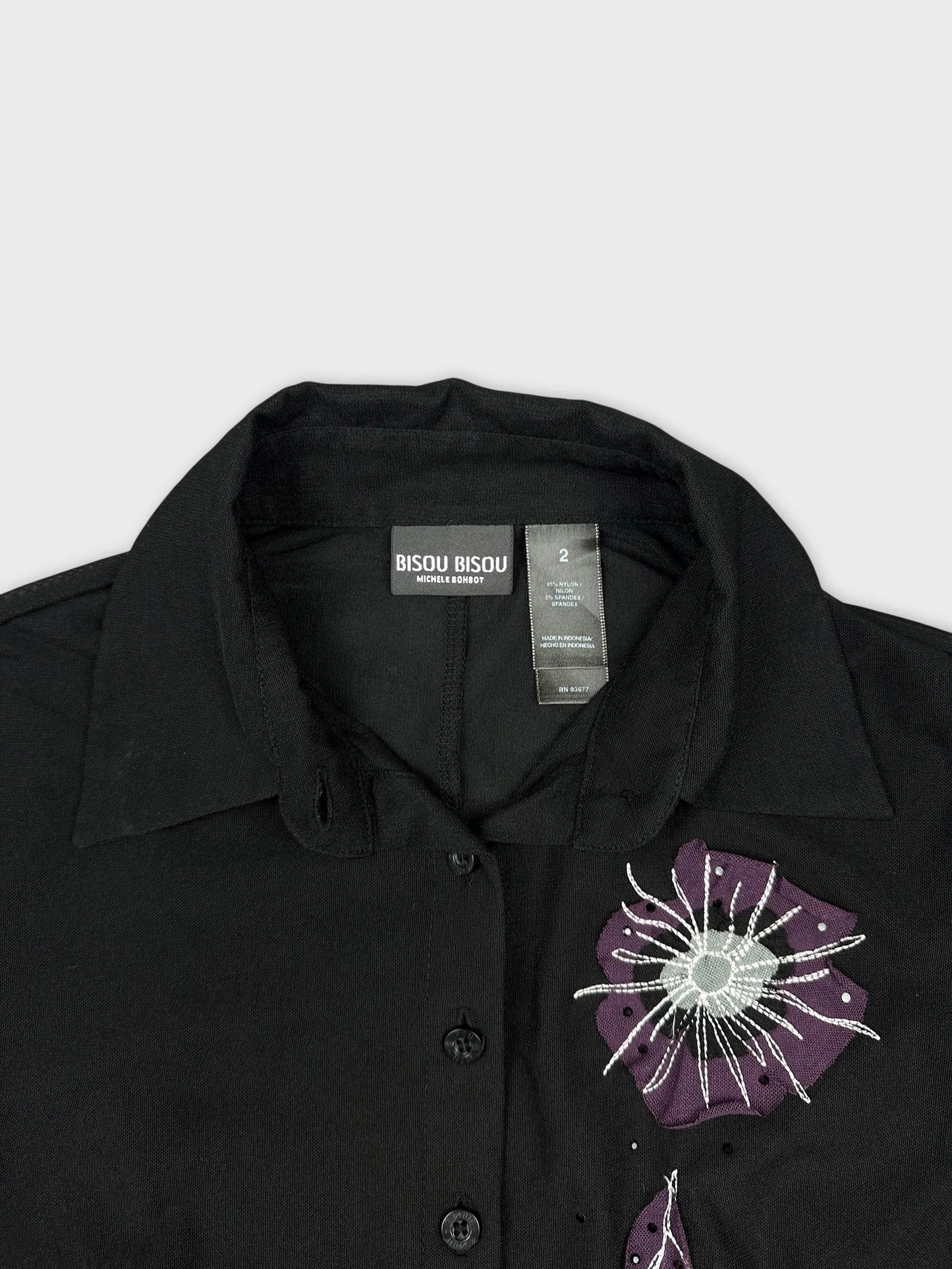 Detail view of a black long sleeve top with purple floral embroidery.