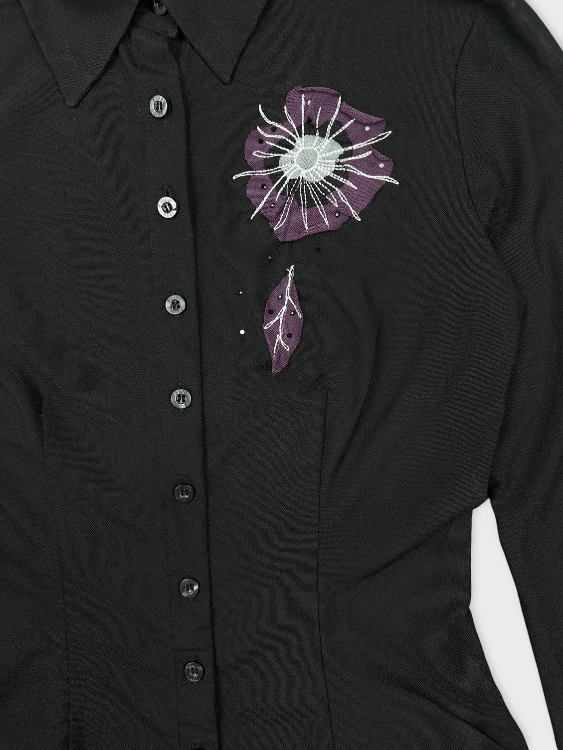 Detail view of a black long sleeve top with floral embroidery.