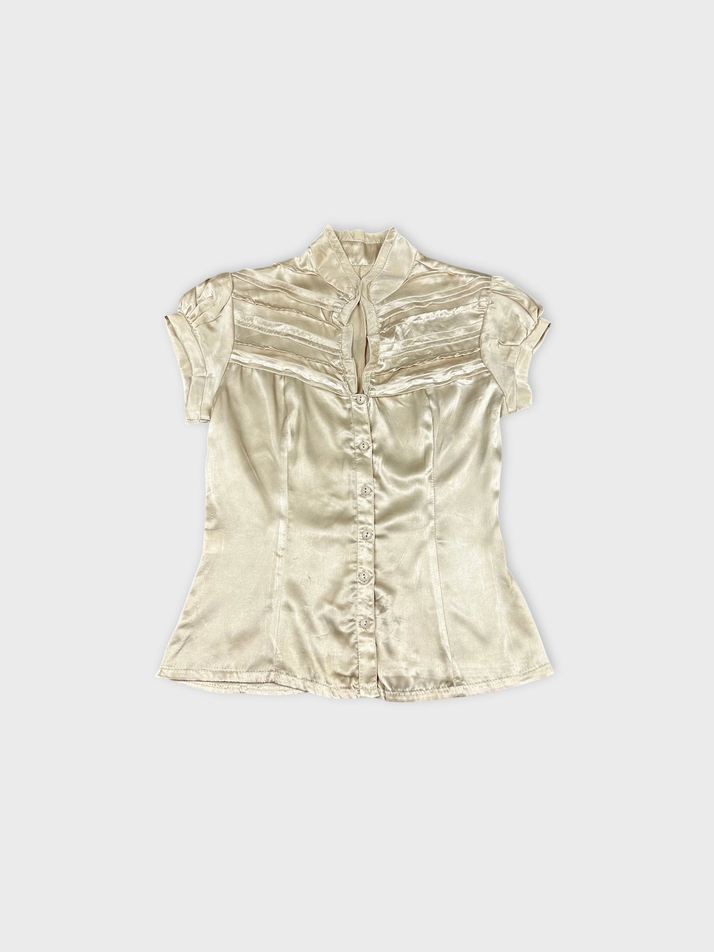 Front view of a short sleeve button up shirt in cream color with pleated detail.