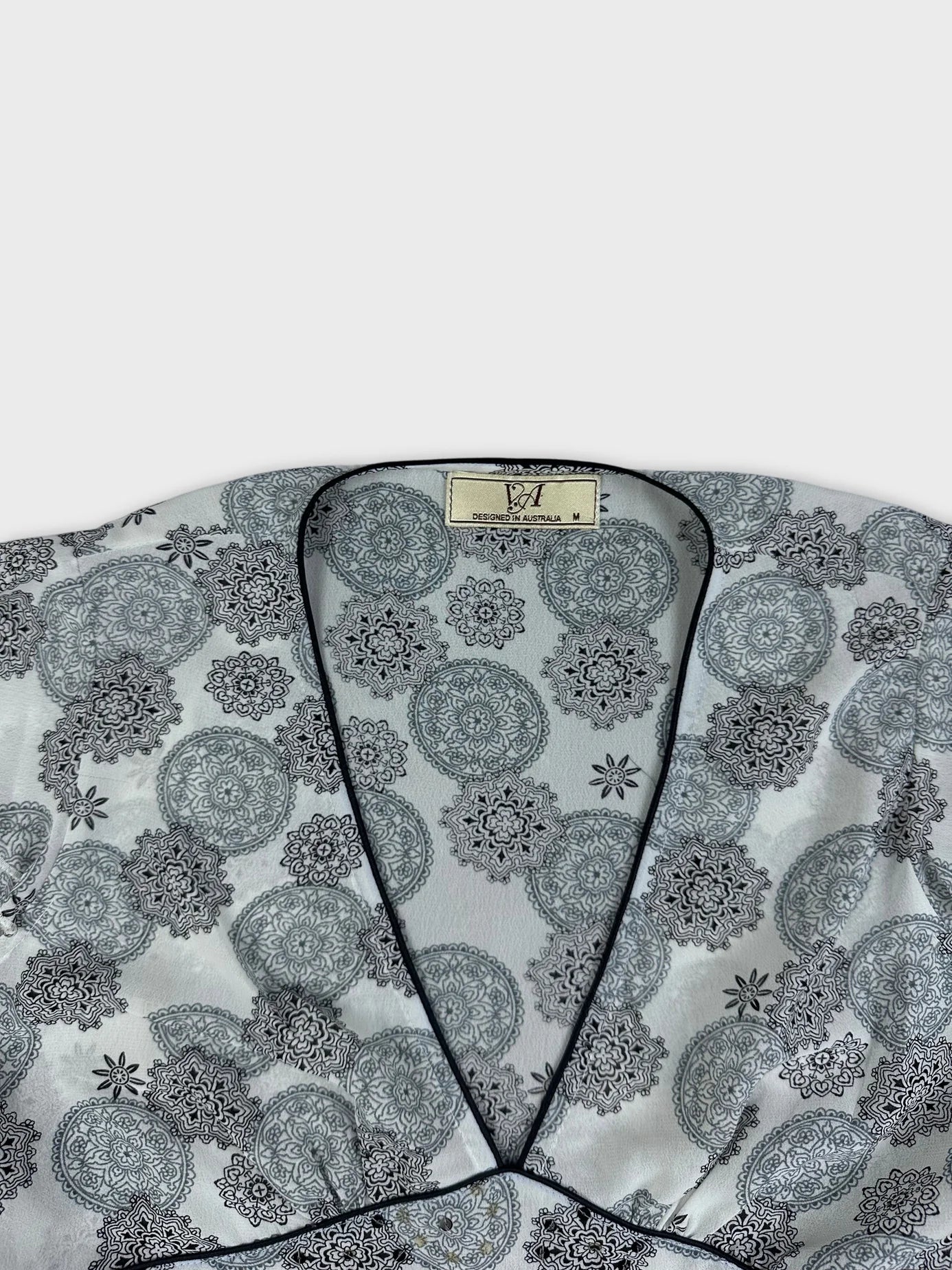 Detail view of a short sleeve top in white with black paisley pattern.