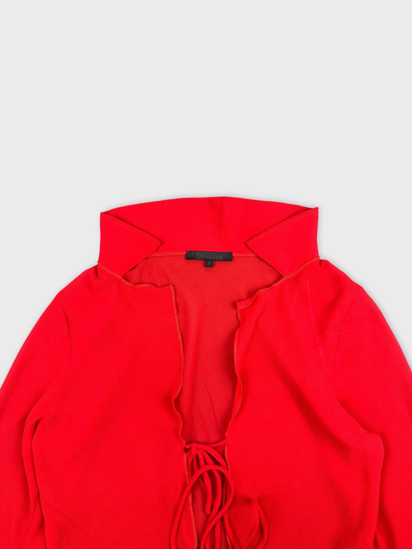 Detail view of a red long sleeve shirt with a ruffled neckline.