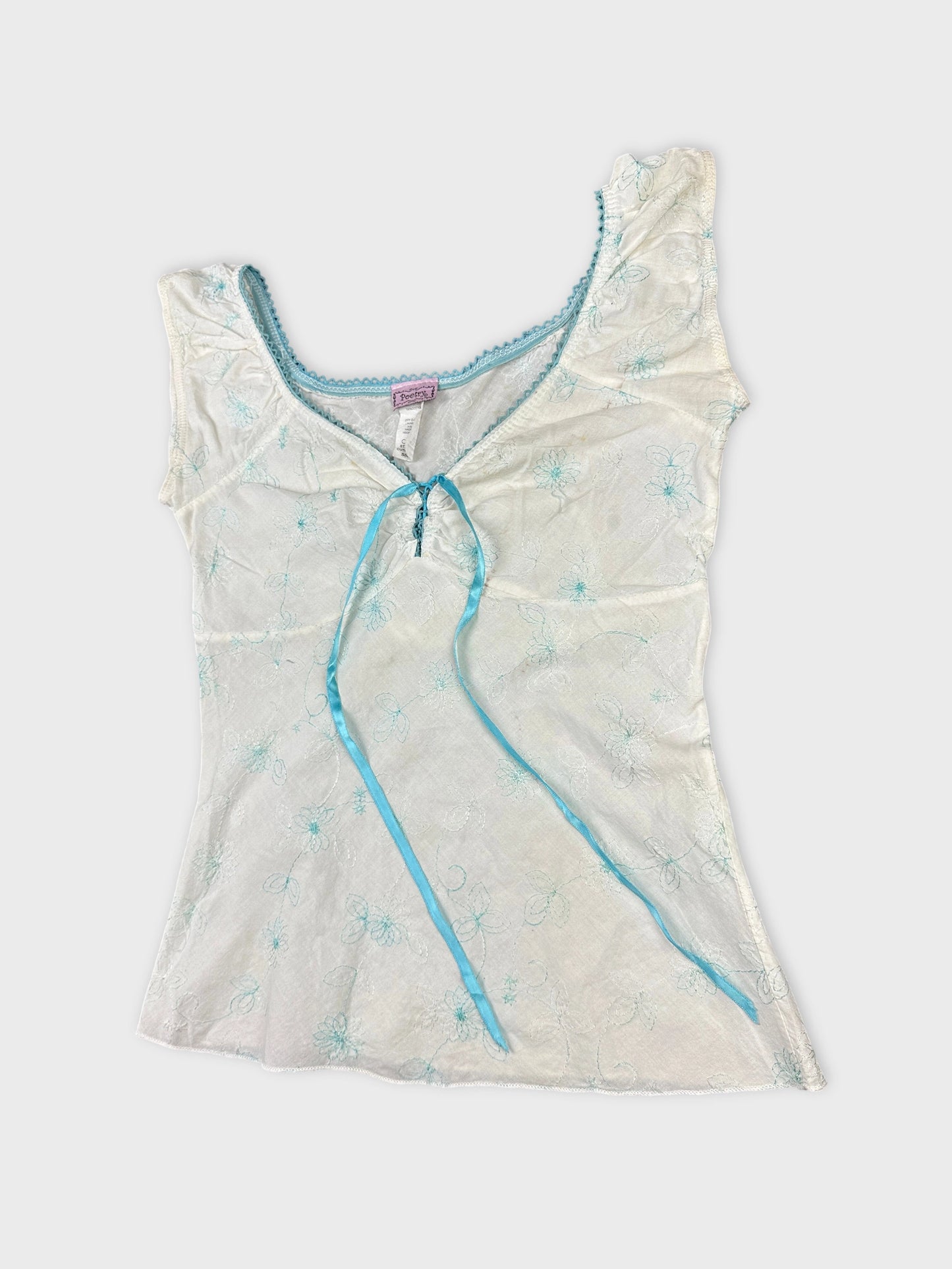 Detail view of a short sleeve top in white with blue floral embroidery.