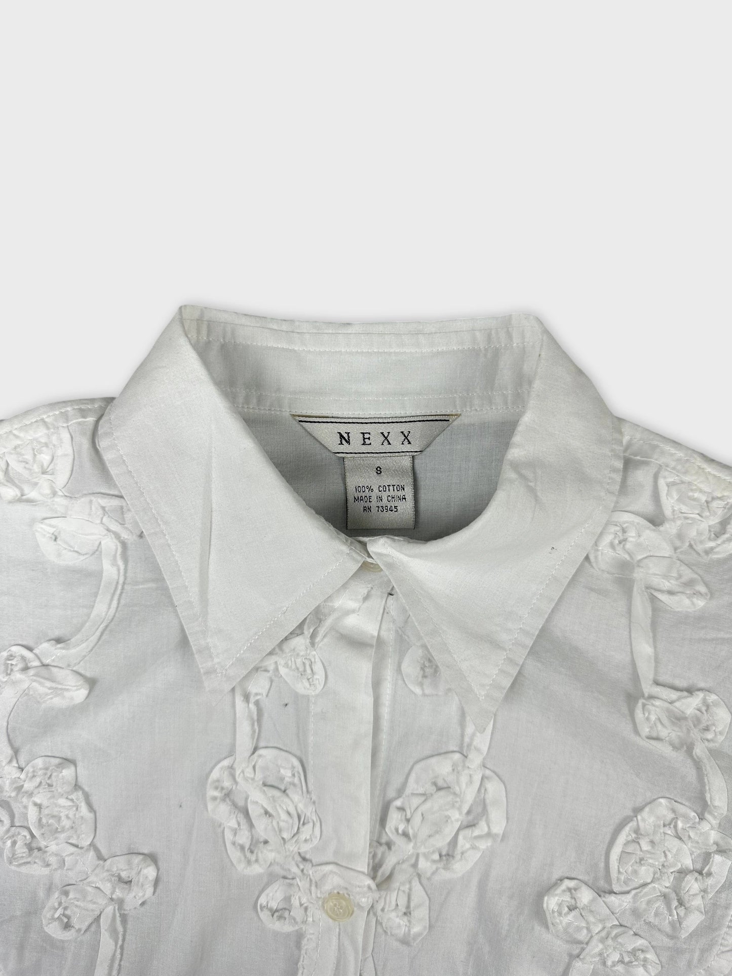 Detail view of a white short sleeve top with floral embroidery.