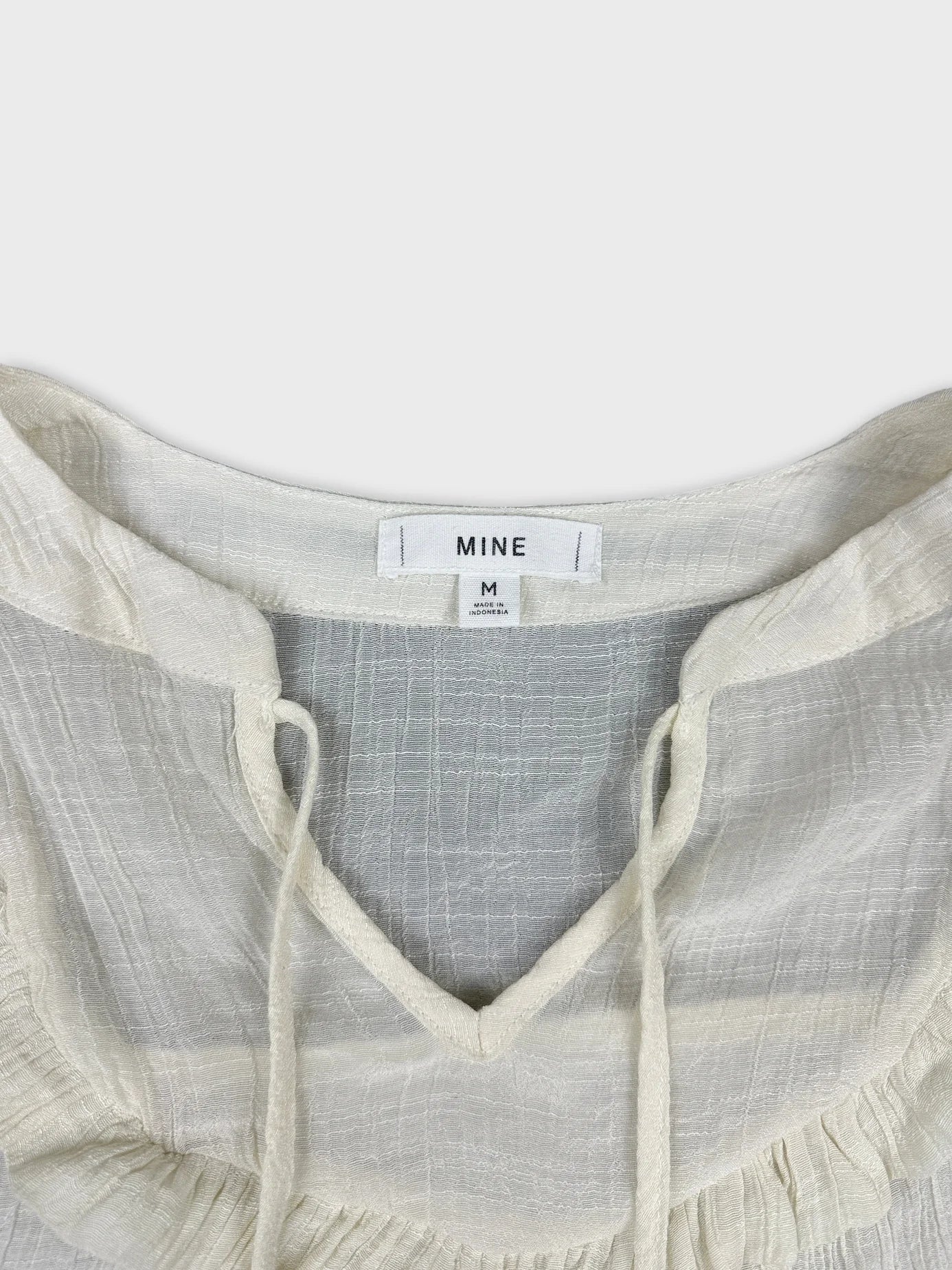 Detail view of a cream short sleeve top with a ruffled neckline