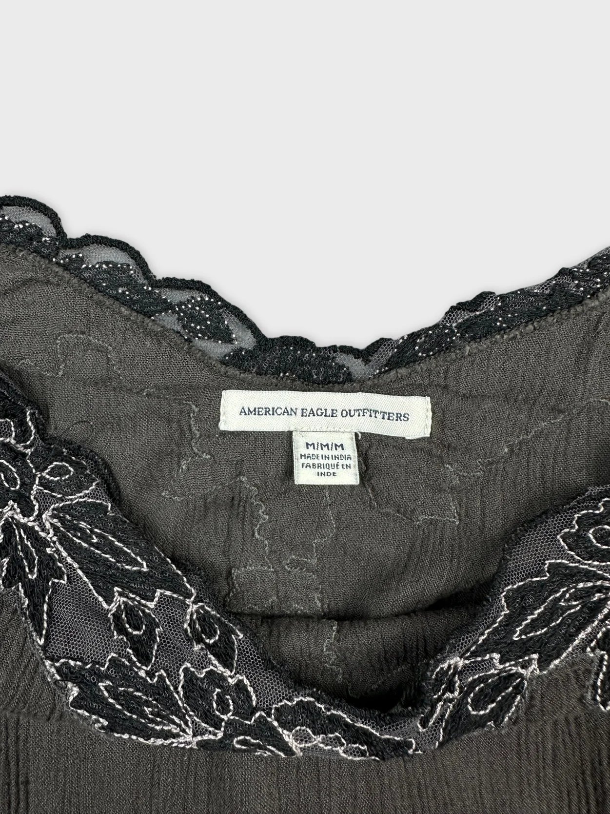 Detail view of a black women's top featuring lace trim and textured fabric.