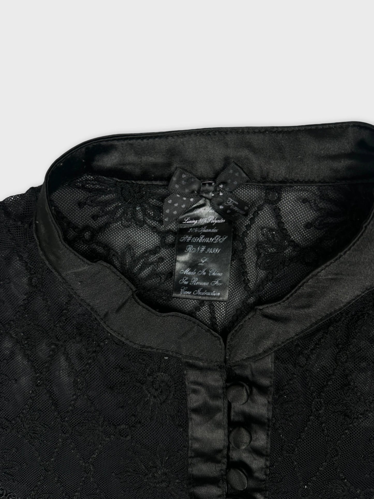 Detail view of a black upper body shirt featuring lace trim and a collar.