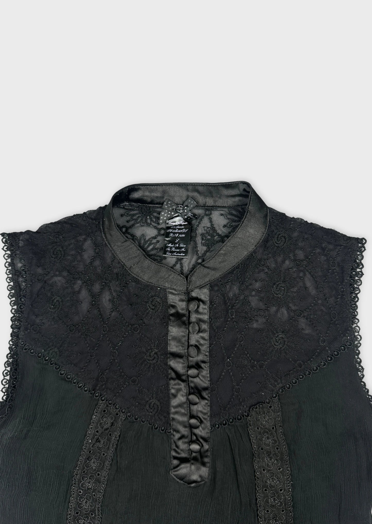 Detail view of a black upper body shirt featuring lace and button details.