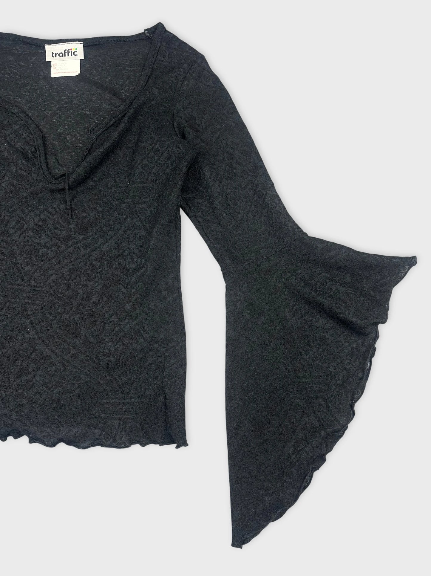 Detail view of a black long sleeve top with bell sleeves and textured pattern.