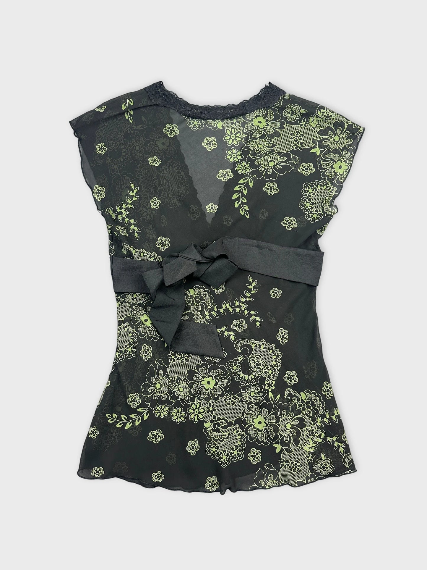 Back view of a black vintage top with green floral prints and bow detail.