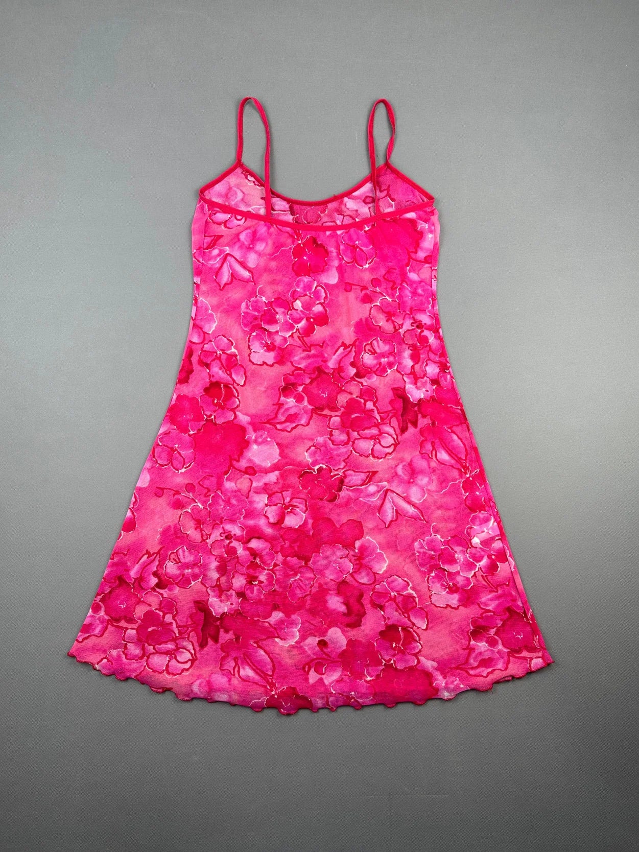 Back view of a pink floral dress with thin straps and scalloped hem.