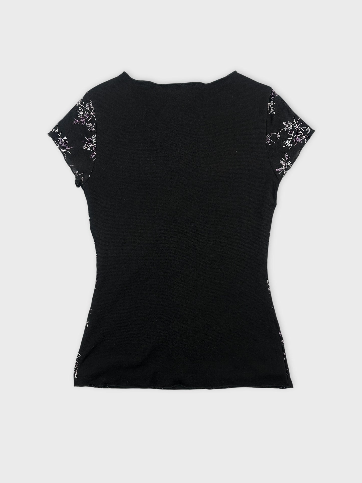 Back view of a black women’s top with floral embroidered sleeves.