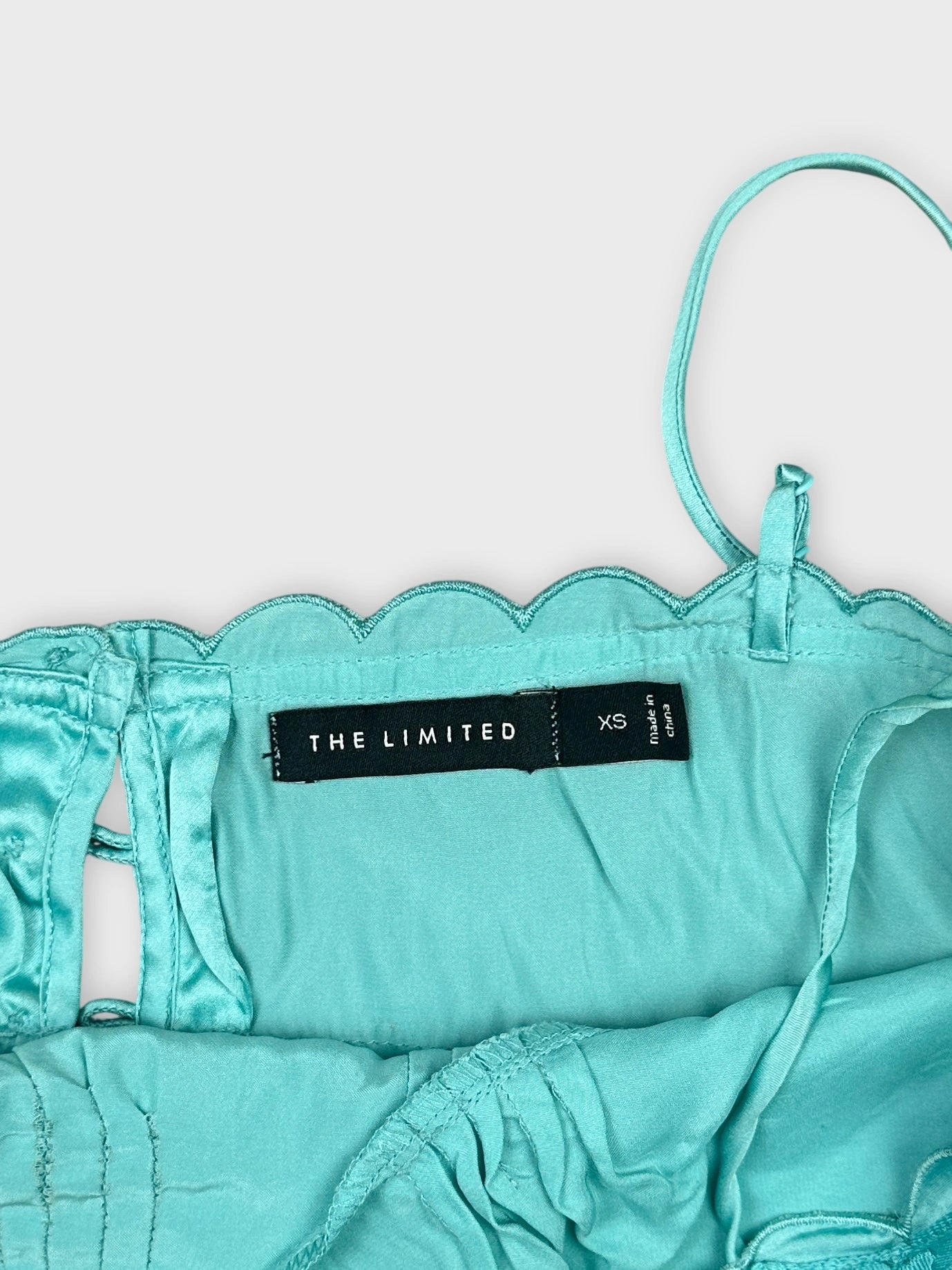 Detail view of a teal upper body top featuring scalloped trim.