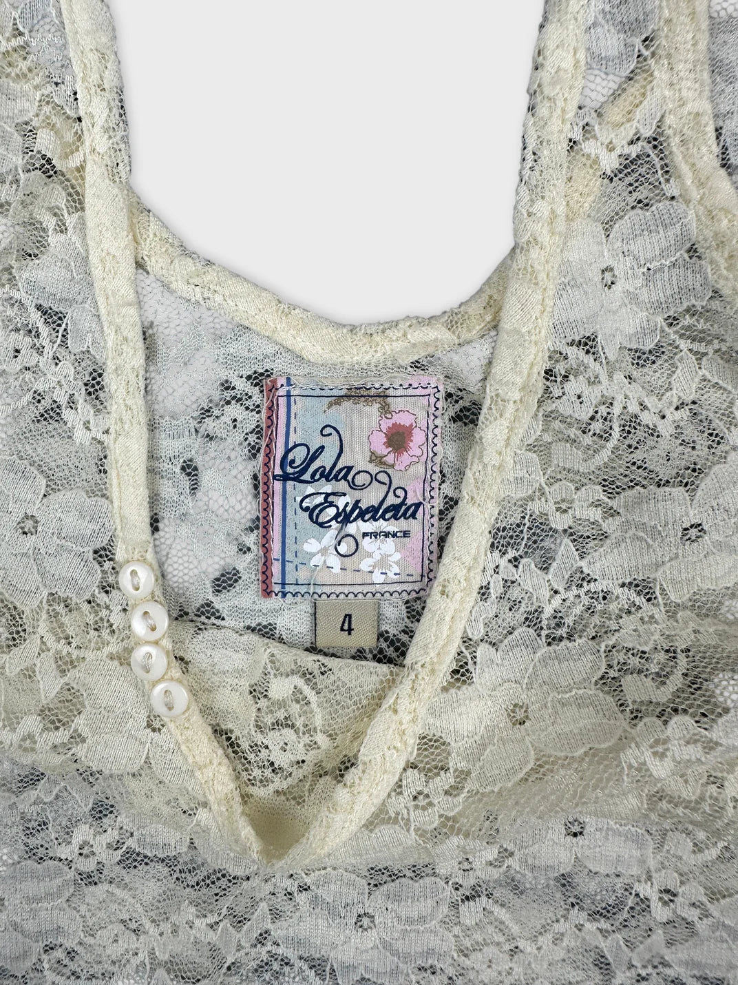 Detail view of an ivory lace top featuring a floral pattern and button details.