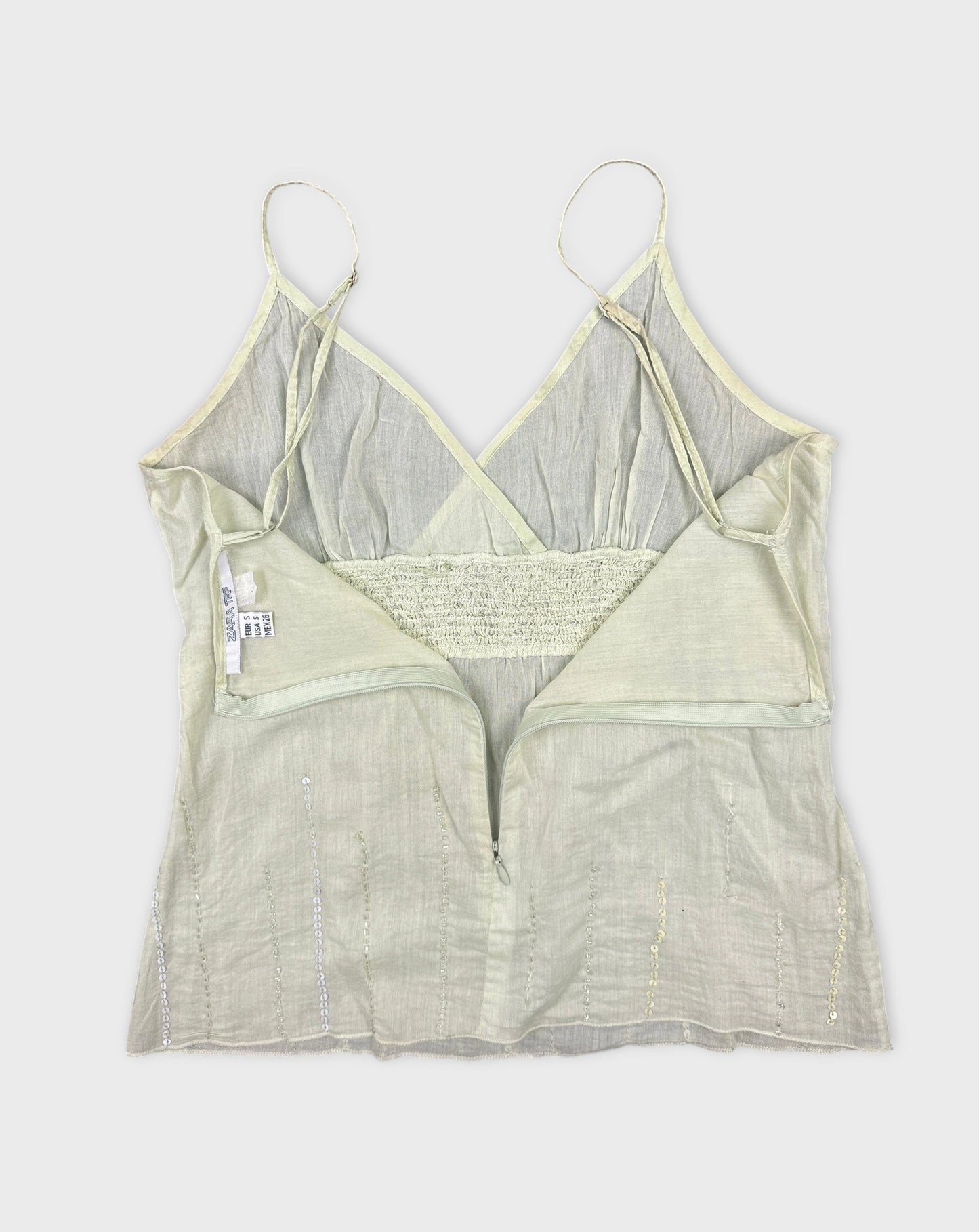 Detail view of a light green women's top with a zip and sequined accents.