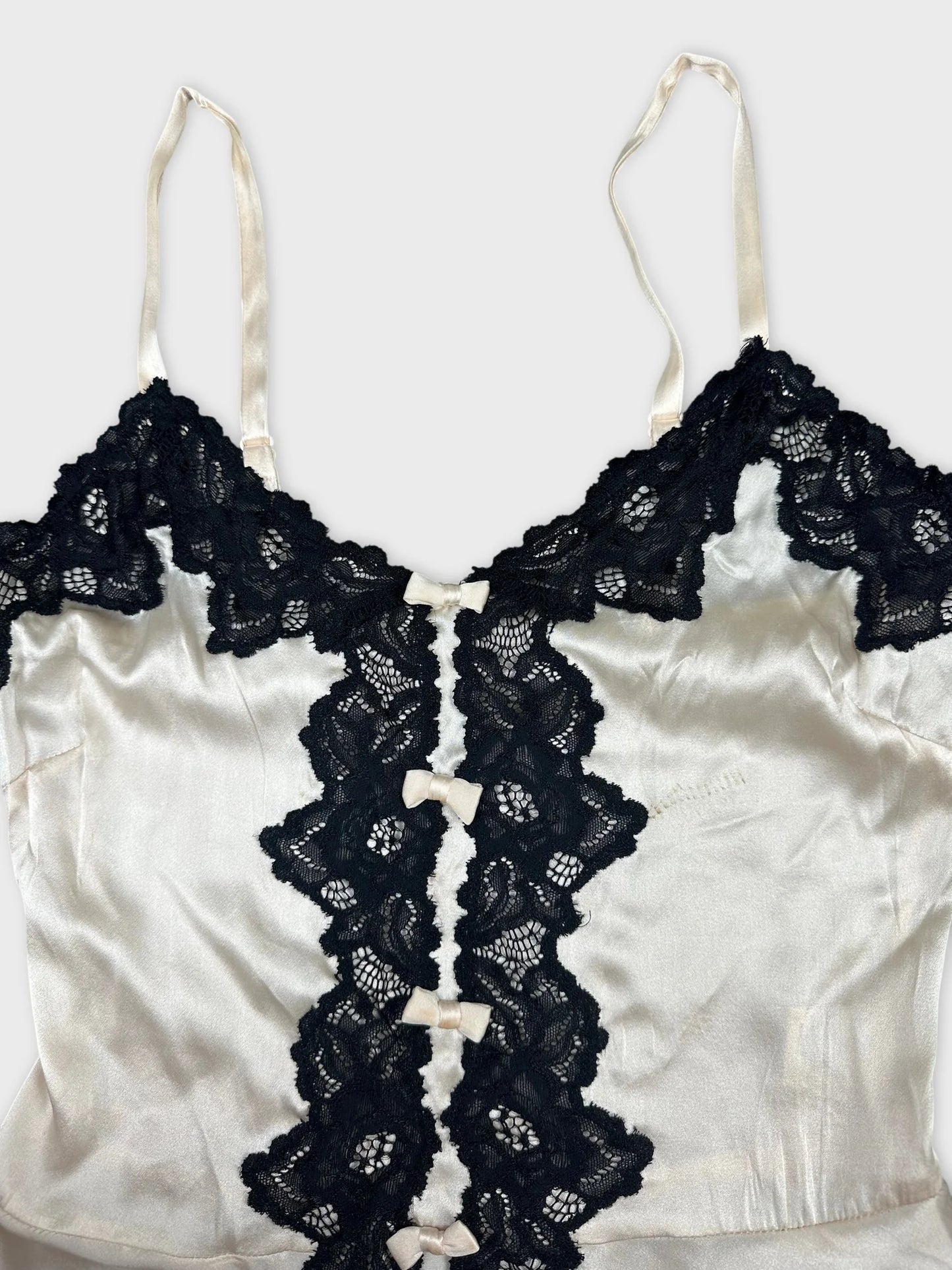 Detail view of a women’s top featuring a cream fabric with black lace trim.