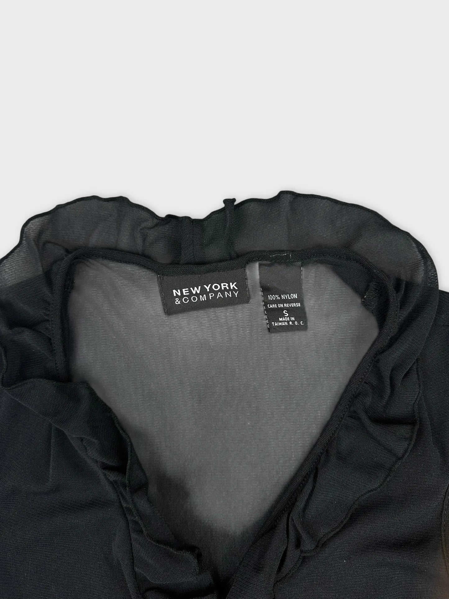 Detail view of black top featuring ruffled neckline from New York & Company.