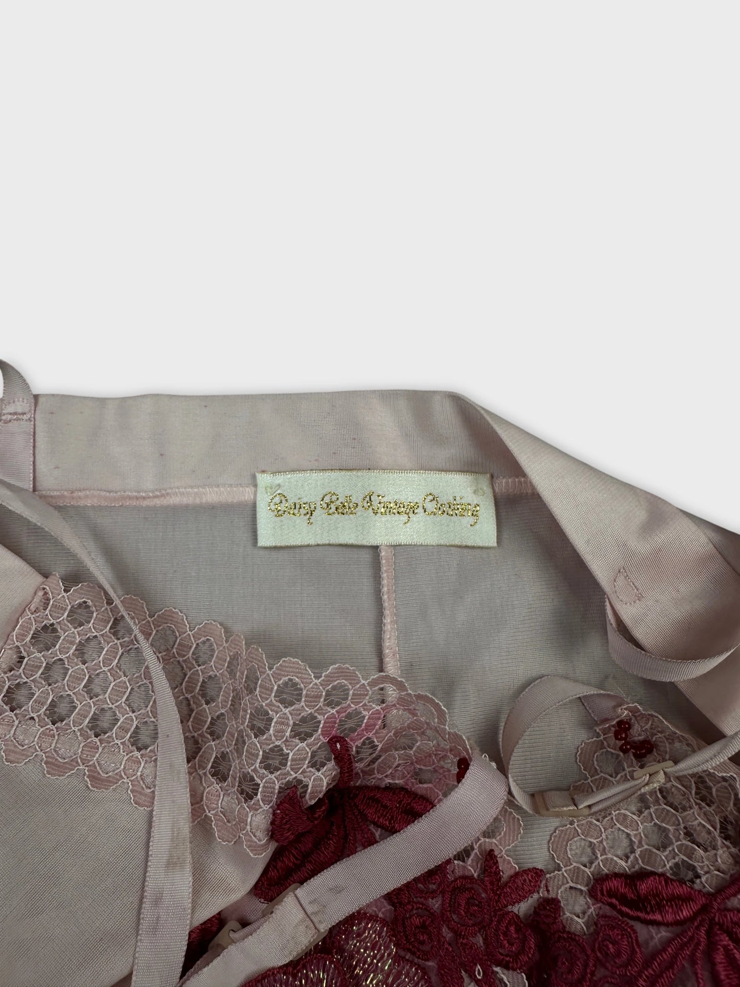 Detail view of a pink vintage top featuring lace trim and intricate embroidery.