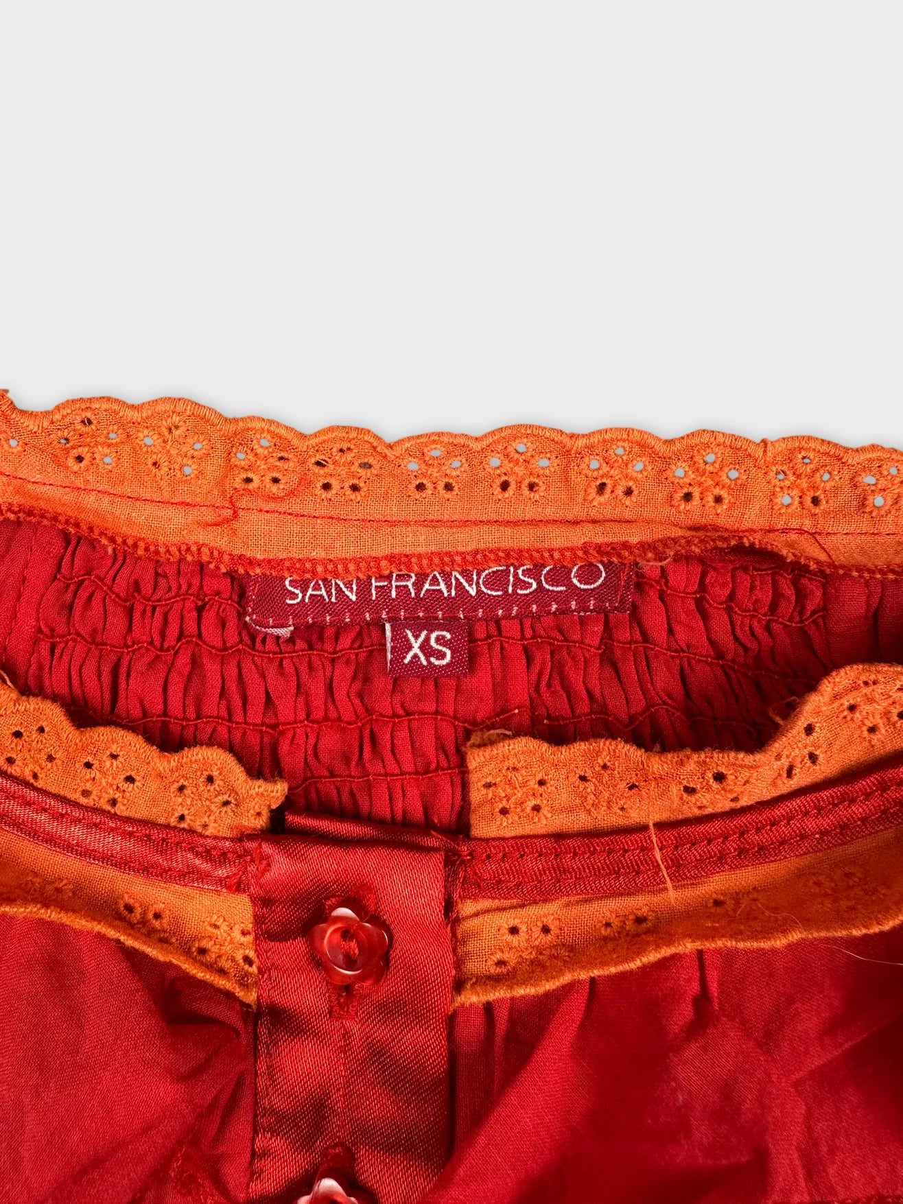 Detail view of a red top featuring orange lace trim and button detail.