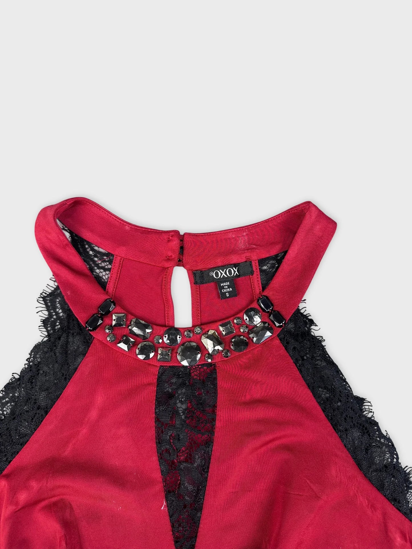Detail view of a red upper body top with black lace trim and embellishments.