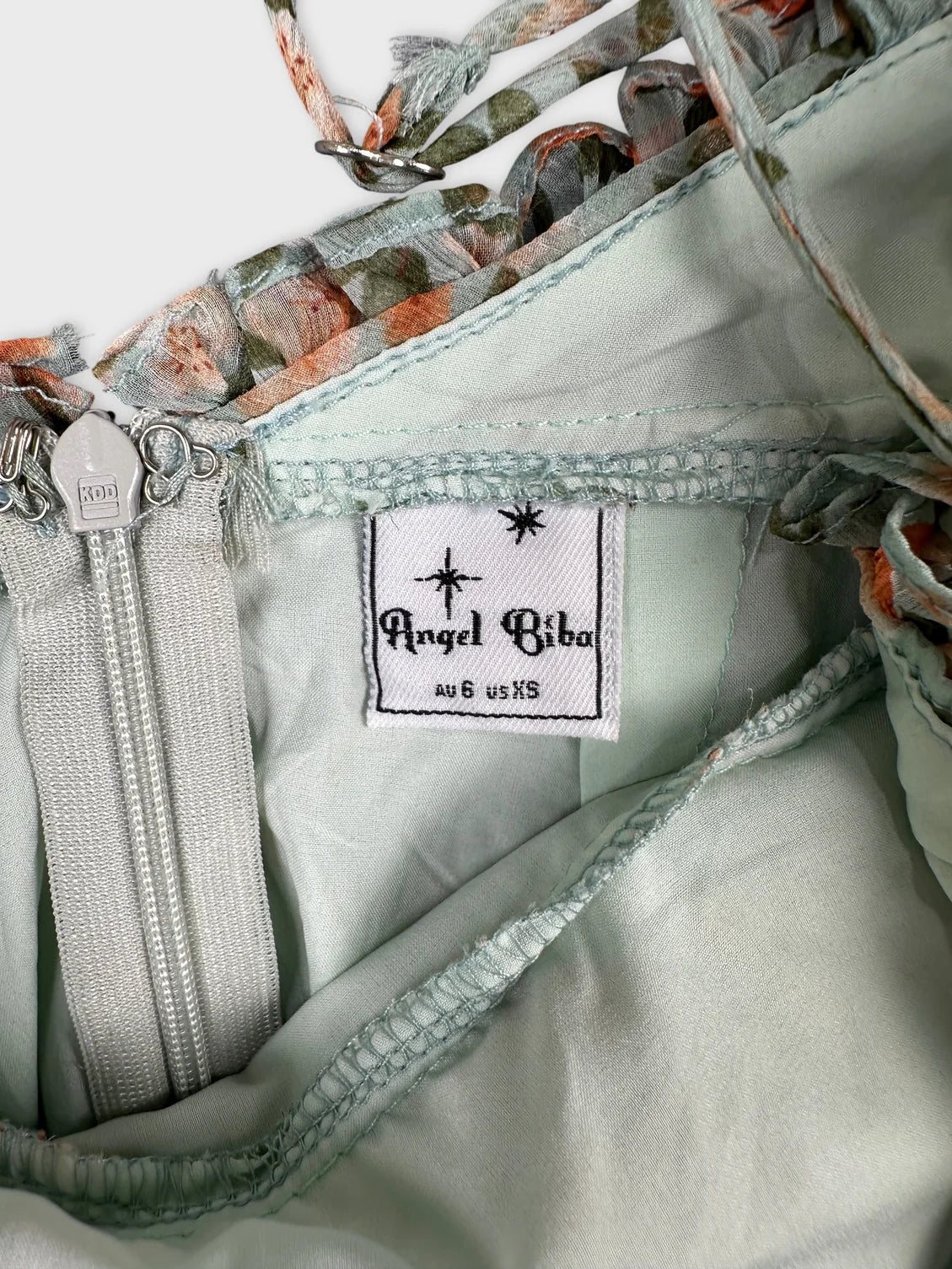 Detail view of a light green vintage top featuring floral trim and zipper.