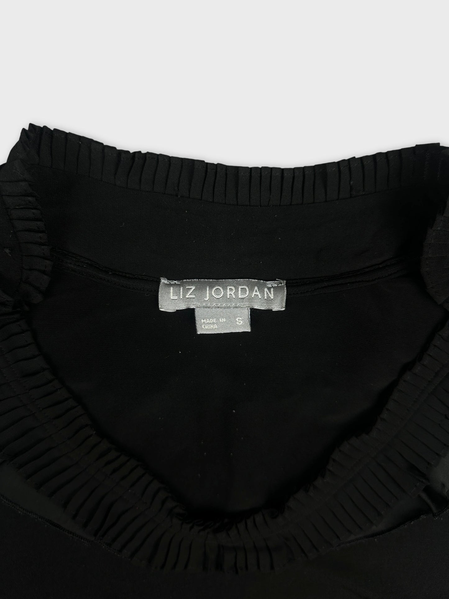Black top with ruffled neckline, detail view.