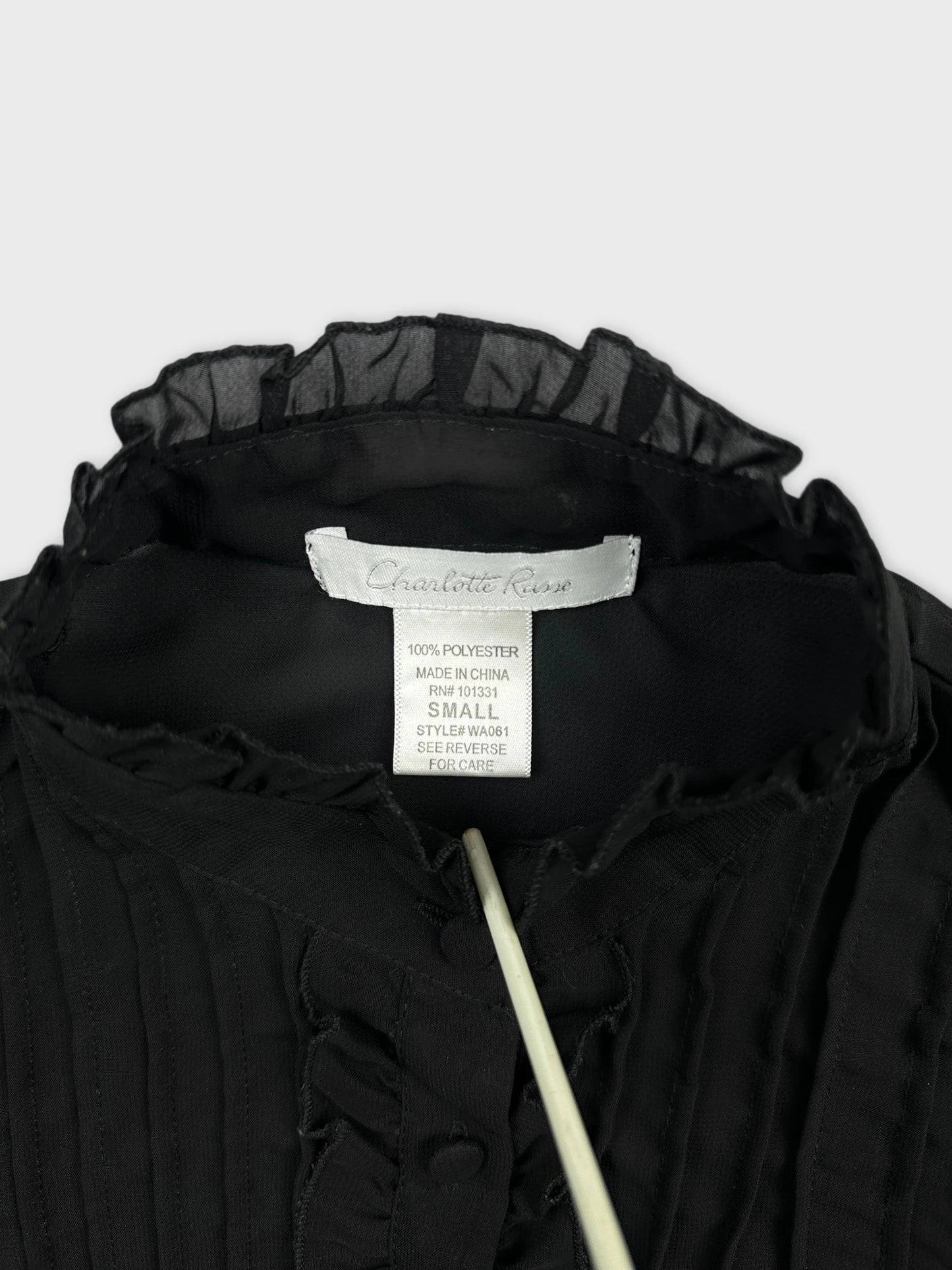 Detail view of a black vintage top featuring ruffled trim and buttons.