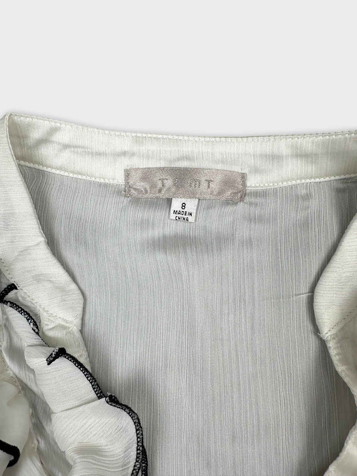 Detail view of a white vintage upper body top with ruffled trim.