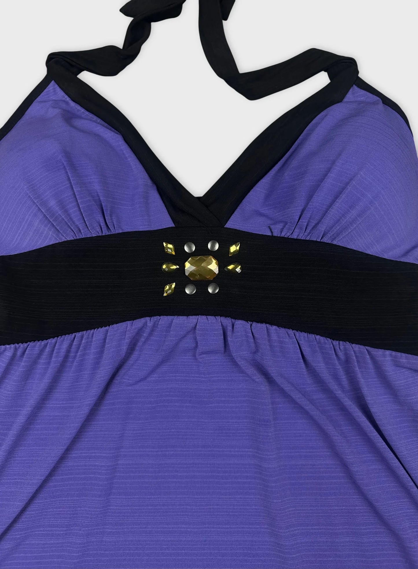 Detail view of a purple women's top featuring a black band and embellishments.